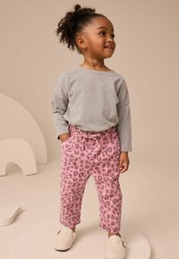 Grå långärmad skjorta kombinerad med rosa leopardmönstrade byxor; byxorna har ett elastiskt midjeband och sidofickor, tillsammans med vita tofflor.