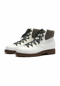 Stivali da trekking bianchi in pelle con risvolto in lana grigia, lacci neri e occhielli in metallo; presentano una suola marrone robusta con design della punta arrotondata.
