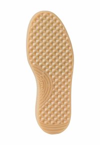 Semelle de chaussure avec motif de grip texturé présentant de petits clous pyramidaux et un logo de marque près de la zone de la voûte plantaire en beige clair.