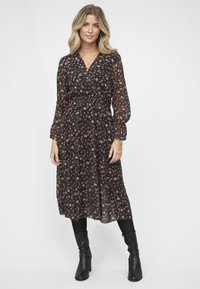 Svart blomstermønstrete kjole med lange puffede ermer, en omslagsdesign og en innsnørt midje. Har små røde og hvite blomster og et flytende skjørt.