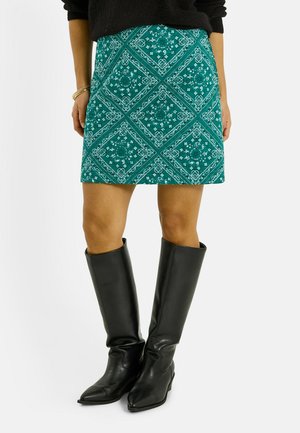 Falda con estampado en tonos verde azulado con diseño de diamantes, combinada con botas negras de cuero hasta la rodilla, textura suave y silueta ajustada.