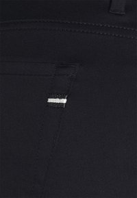 Svarta tygbyxor med en stilren, slät textur, med en sidoficka som har en vit och silverrandig detalj.