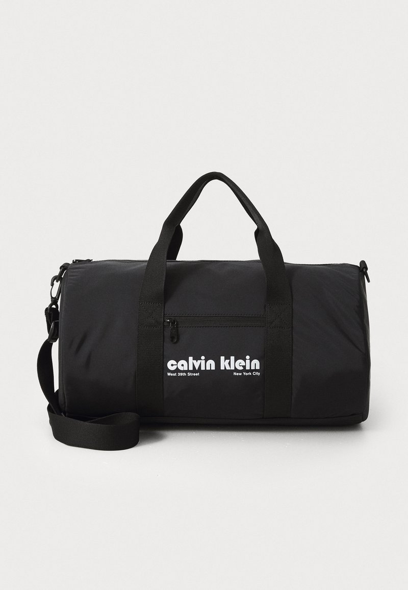 Black duffel bag made of durable fabric. Features dual handles and a detachable shoulder strap. Front zip pocket and brand logo prominently displayed.