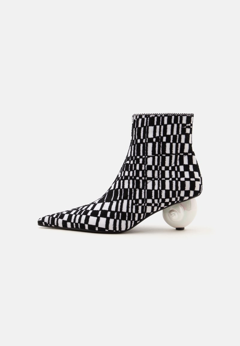 Bottine à carreaux noir et blanc avec bout pointu et talon sculptural blanc rond sur fond gris.
