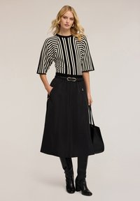 Zwart-wit gestreepte gebreide top met korte mouwen, gecombineerd met een lange zwarte rok, gecorrigeerd met een riem en een zwarte handtas.