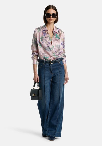 Silkkblus i rosa med gröna och lila blommönster, tillsammans med vida blå denimjeans och en liten svart handväska.