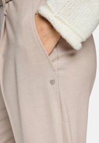 Light beige trousers with a smooth texture, featuring a side pocket and a small silver accent button detail.