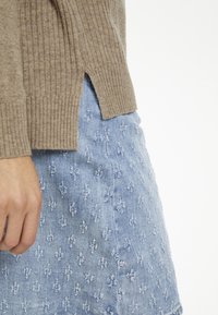 Beżowy sweter w prążki z bocznymi rozcięciami, zestawiony z jasnoniebieską spódnicą dżinsową z fakturowanym kwiatowym wzorem.