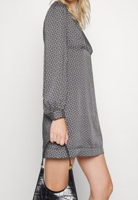 Vestido de estampado en blanco y negro con mangas largas y un corte holgado, complementado con un bolso negro con grabado de cocodrilo.