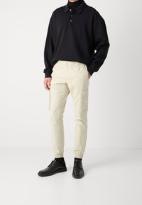 Černé volné polo tričko s třemi knoflíky, kombinované s krémovými cargo kalhotami s elastickým pasem a bočními kapsami. Doplňeno černými botami.
