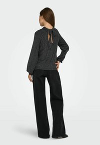 Blusa nera texturizzata con maniche lunghe e chiusura sul retro a occhiello legata con un nastro. Abbinata a pantaloni neri a gamba larga, per un mix di stili.