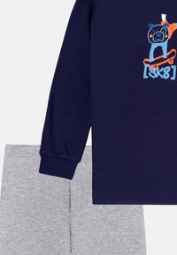 Marineblauwe longsleeve shirt met een hondenafbeelding in blauw en oranje, gecombineerd met grijze shorts. De stof lijkt zacht met een gladde textuur.