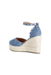 Espadrillas con zeppa in denim, punta tonda, cinturino alla caviglia decorato con borchie metalliche e piattaforma in juta intrecciata. Tessuto blu e suola neutra.