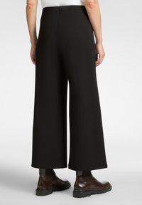 Zwarte wijde broek met een gladde textuur en een hoge taille, gecombineerd met bruine enkellaarzen met een chunky zool.