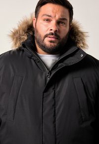 Svart parkas med foder av konstgjord päls i huvan, med dragkedjestängning och två framfickor, tillverkad av ett smidigt, vattenavvisande material.