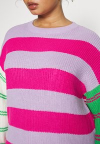 Chunky stickad tröja med horisontella ränder i lavendel, klar rosa och grön. Rundad halsdesign med ribbad textur på ärmslut.