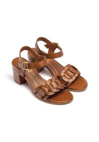 Sandales en cuir brun avec un design de bride tressée, des brides autour de la cheville et un talon épais. Texture lisse, bout ouvert et boucle réglable.