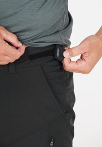 Schwarze Hose mit strukturiertem Finish, ausgestattet mit einem Klettverschlussverstellriemen an der Taille und einer seitlichen Reißverschluss-Tasche.