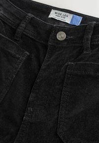 Plačios kojos, aukšto liemens juodos korduroy kelnes su priekinių kišenių ir metaliniu susagstymu. Etiketė, nurodanti "Plačios kojos aukštas liemuo."