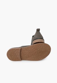 Scarpa in suede grigia con suola in sughero testurizzata. Presenta un accento in pelle marrone e un anello sul tallone per facilitare l'indossamento.
