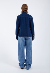 Dunkelblaue Jeansjacke mit langen Ärmeln und Knopfmanschetten, kombiniert mit locker sitzenden hellblauen Jeans. Einfaches Design, lässige Passform.