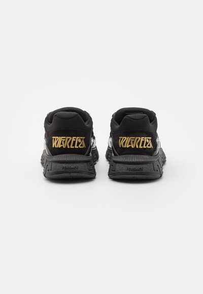 Black sneakers with a textured upper, featuring bold gold lettering on the heel and a thick black sole. The design is sleek and modern.