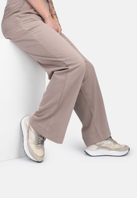 Beige wijde broek met een gladde textuur, gecombineerd met lichte sneakers met een mesh- en suède ontwerp in neutrale tinten en veters.