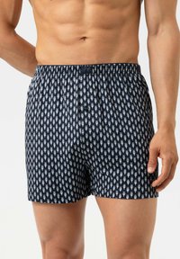 Boxer bleu marine en coton, présentant un petit motif blanc répétitif. Taille élastique avec fermeture par bouton.
