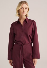 Bordeaux košile s dlouhým rukávem, klasickým límcem a elegantním designem. Hladká textura, doplněná o odpovídající kalhoty s šňůrkovým pasem.