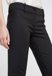 Czarne, dopasowane spodnie wykonane z gładkiego materiału. Posiadają dopasowany pas z pętlami na pasek, boczne kieszenie oraz wąski krój nogawek. Minimalistyczny design.