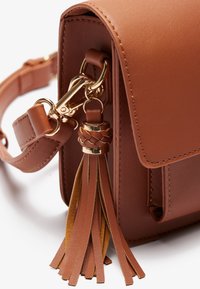 Brown faux leather handbag with a flap, gold hardware, braided tassel detail, and adjustable strap. Compact design with smooth texture.