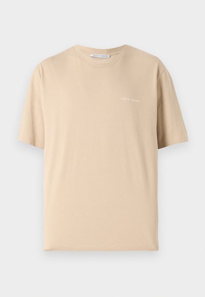 Beige kortermet T-skjorte laget av myk bomull. Har rund hals og minimalistisk tekst som sier "TIGER OF SWEDEN" i hvitt.