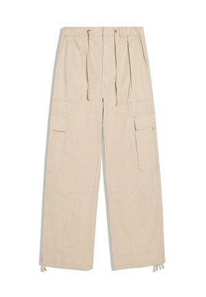 Beige Cargo-Hose mit weitem Bein, Kordelzug in der Taille, mehreren vorderen und seitlichen Taschen sowie verstellbaren Bändern an den Knöcheln.