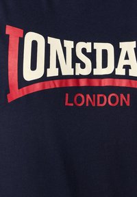 Marinblå bomulds t-shirt med stor hvid og rød tekst, der siger "LONSDALE" over "LONDON," med en glat tekstur og afrundet design.