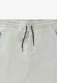 Lichtgrijze joggers van een gestructureerde stof, met een elastische tailleband met een zwarte trekkoord en ritszakken aan de zijkanten.