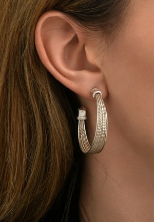 Boucles d'oreilles en argent en forme de hoop avec un design texturé et une petite pierre claire en accent, suspendues au lobe de l'oreille sur un fond neutre.