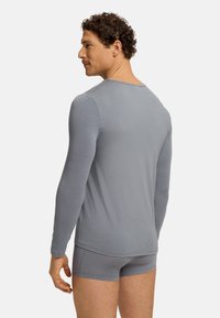 Grijs shirt met lange mouwen, gemaakt van een zachte, lichte stof, met een ronde halslijn en een strakke pasvorm. Gecombineerd met grijze boxershorts.