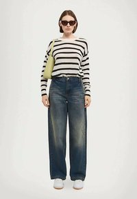 Svijetlozeleni džemper sa crno-bijelim prugama, plave široke traperice, bijele tenisice i svijetlozelena torba; model nosi naočale za sunce.