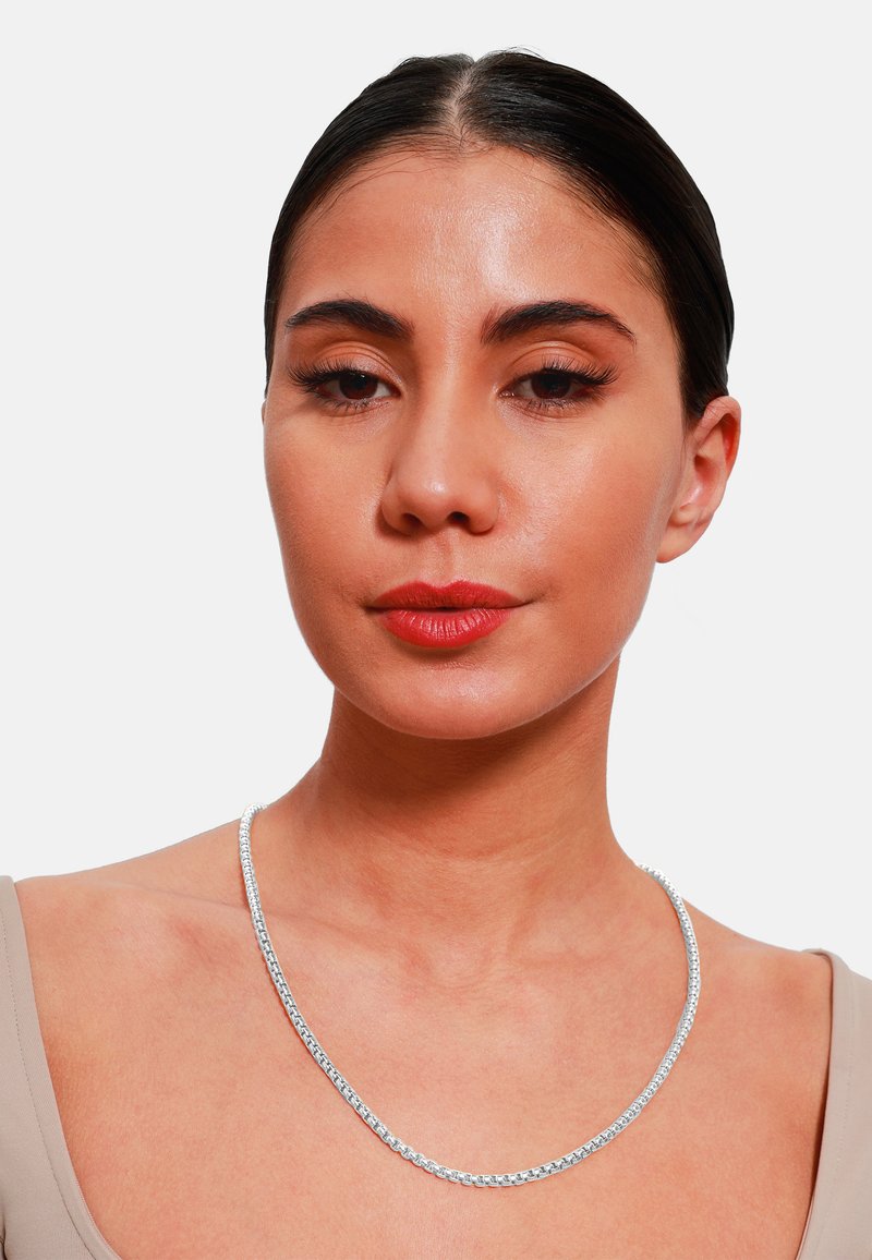 Collana in argento con design a maglie rotonde, texture liscia e finitura lucida, indossata attorno al collo sopra una maglietta dai toni tenui.