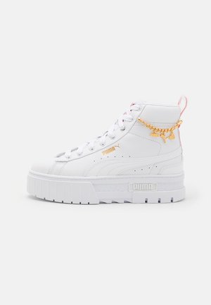 Hvid højtop Puma sneaker med tyk sål, gyldent Puma-logo og kæde med vedhæng nær anklen samt snørelukning.