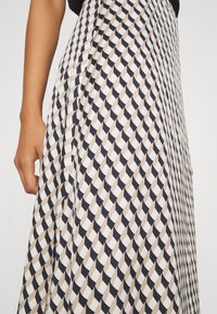 Jupe maxi avec un motif géométrique en marine, beige et blanc. Fabriquée à partir d'un tissu léger au toucher doux et avec un design plissé.