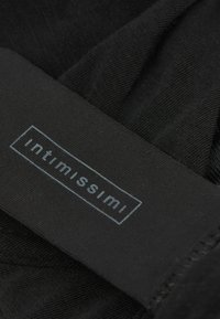 Černá průhledná tkanina s hladkým povrchem a elastickým páskem označeným "intimissimi" v světle modrém písmu.