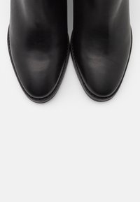 Černé kožené kotníkové boty s špičatou špičkou a hladkým povrchem. Šité detaily podél okrajů a minimalistický design.
