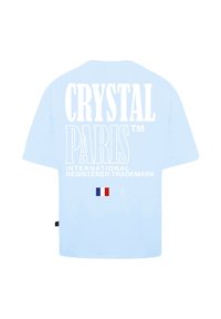 Světle modré bavlněné tričko s bílým potiskem textu "CRYSTAL PARIS™" a malou francouzskou vlajkou níže. Standardní design s krátkými rukávy.