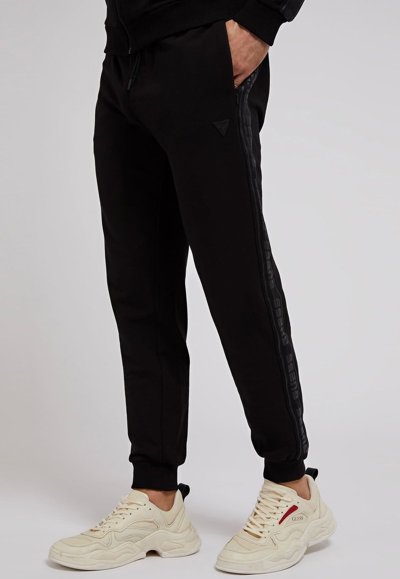 Herren Trainingsanzüge | Guess LOGO BAND Jogginghose schwarz - US00492 Herren Trainingsanzüge | Guess LOGO BAND Jogginghose schwarz - US00492