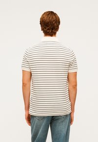 Μπεζ πόλο πουκάμισο με λεπτές καφέ ρίγες, κοντά μανίκια και κλασικό γιακά. Συνδυασμένο με ανοιχτόχρωμο μπλε τζιν. Καθαρός, μίνιμαλ σχεδιασμός.