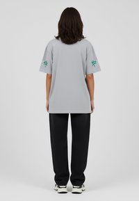 Grijze oversized T-shirt met een gevlochten patroon, voorzien van groene geborduurde accenten op de mouwen, gecombineerd met zwarte ontspannen pasvorm broek.