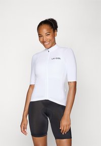 Biela cyklistická dres s krátkym rukávom, predným zipsom a čiernym logom. Vybavené čiernymi cyklistickými šortkami s polstrovaným sedadlom.