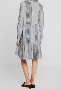 Robe à manches longues présentant un mélange de motifs à rayures noires et blanches et de dessins floraux, avec un ourlet à volants et un col à revers.