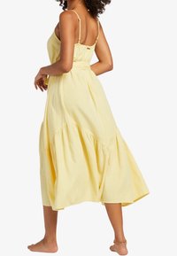 Gelbes, ärmelloses Maxikleid mit dünnen Trägern, einem engen Oberteil und einem mehrstufigen, fließenden Rock. Leichter Stoff mit weicher Textur.